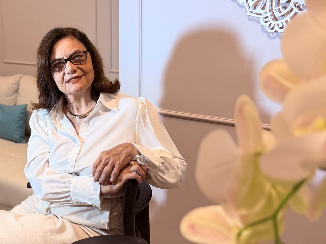 Cristiane Ribeiro sentada em seu consultório, com uma orquídea em primeiro plano